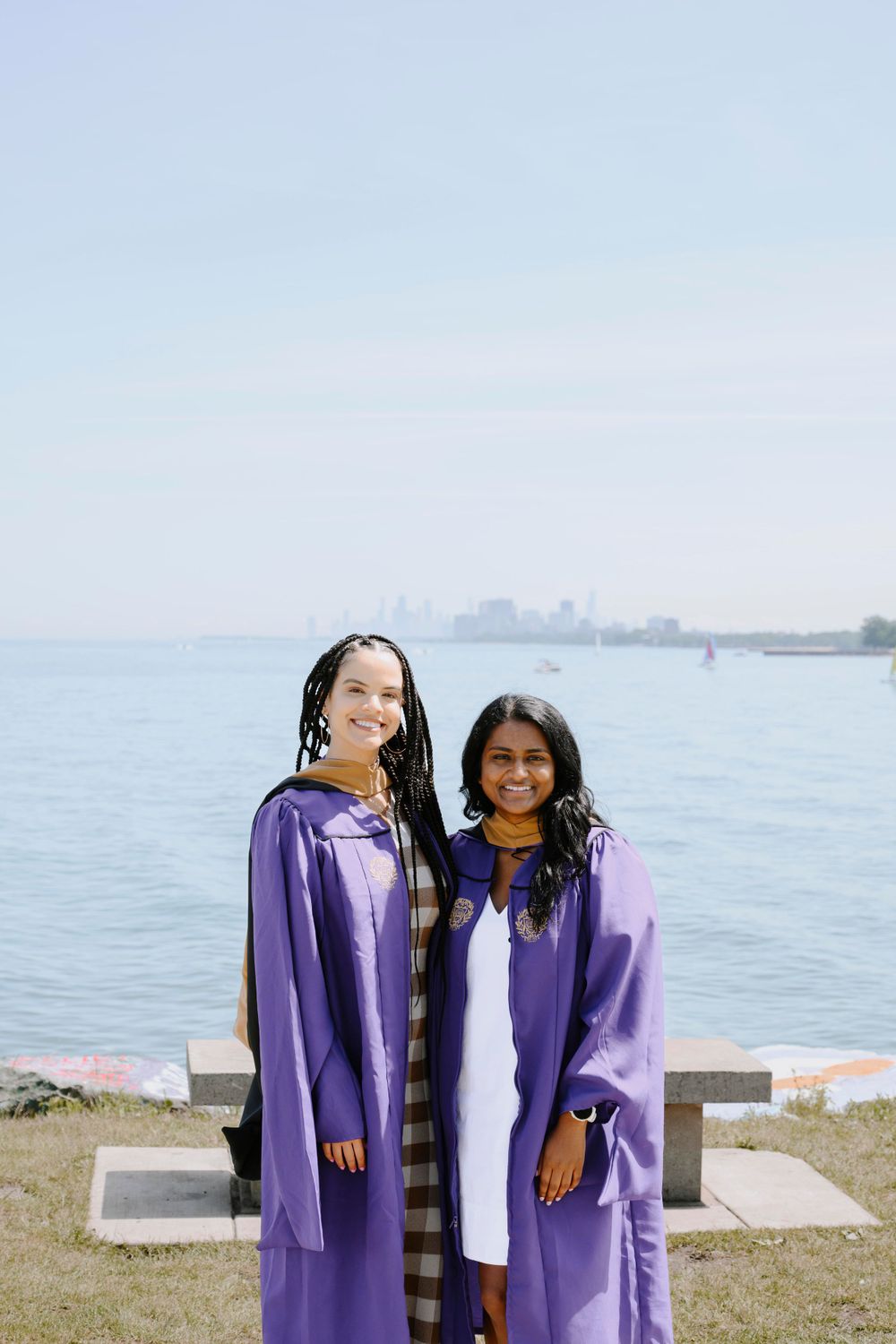 Two graduates in purple gowns by the lake, smiling. Chicago graduation photographer capturing joyful moments