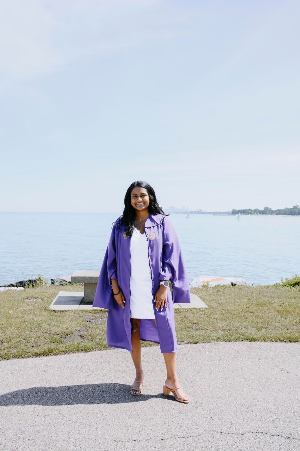 Graduate in purple gown by the lake, smiling. Chicago graduation photographer capturing proud and joyful moment