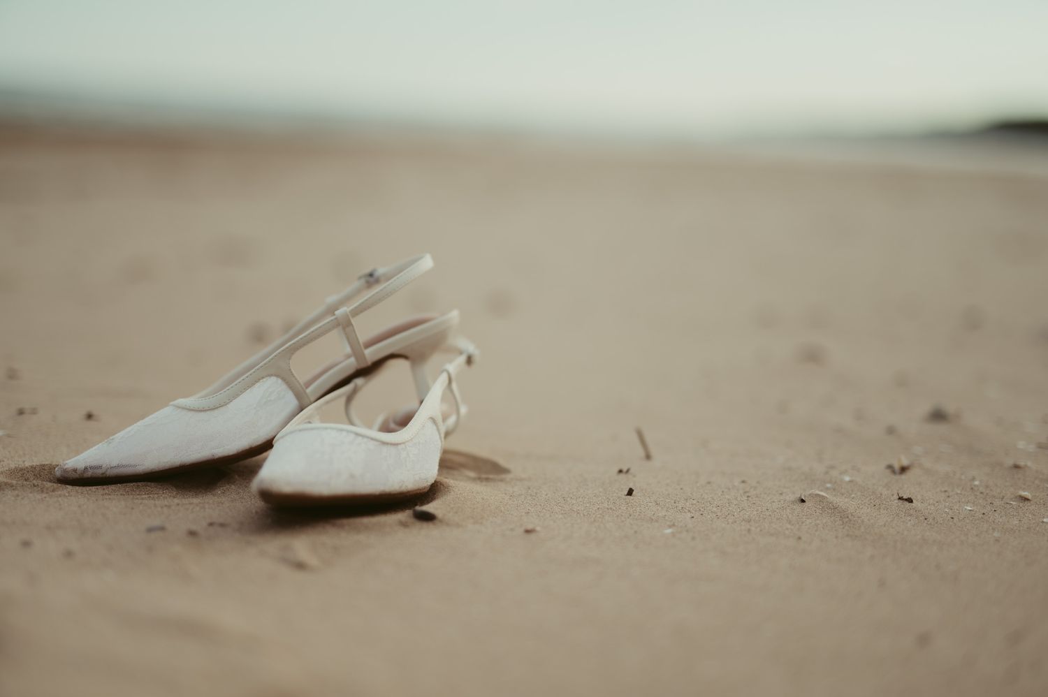White slingback heels resting on sandy beach, elegant bridal shoes on shore of Port Washington, WI beach.