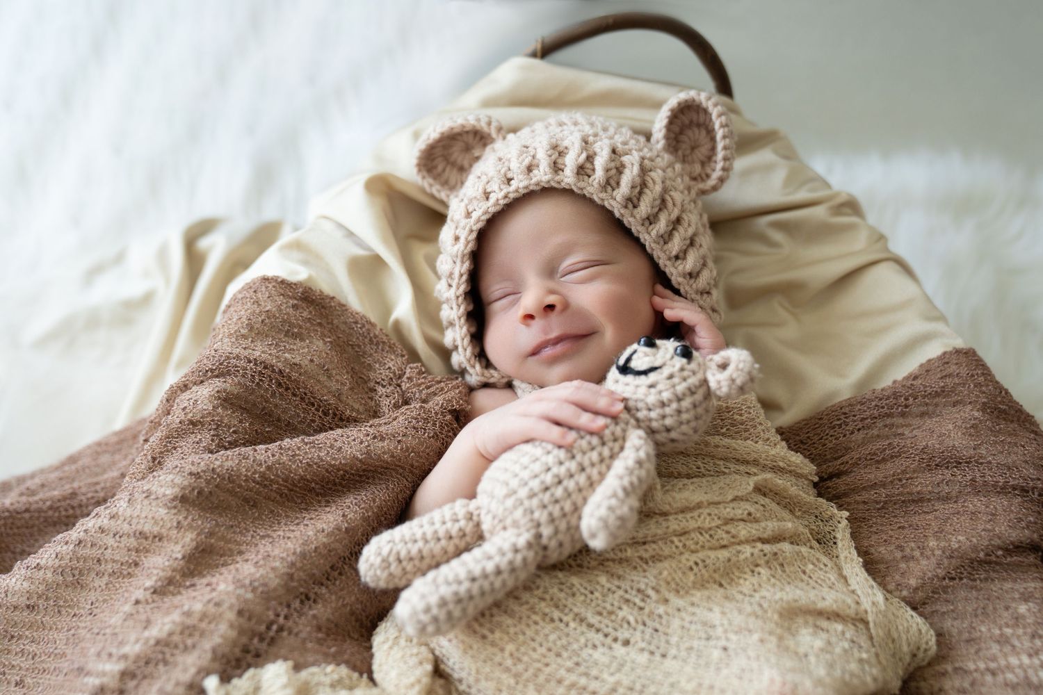 Sleeping baby wearing a knit bear hat cuddles with a plush toy under cozy blankets.