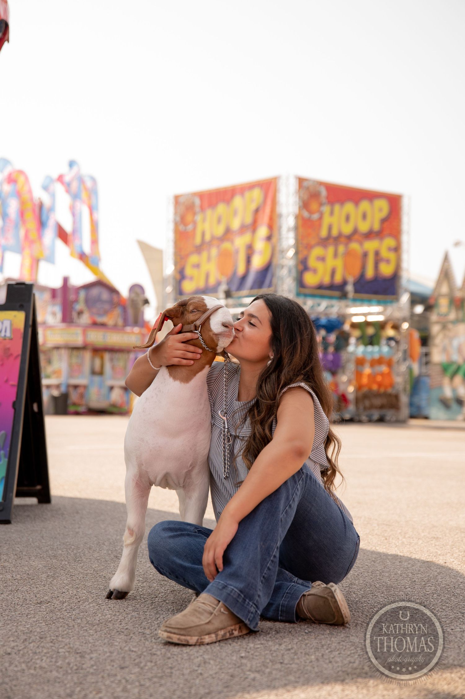 A sweet moment between a white dog and their companion at a carnival with game booths.