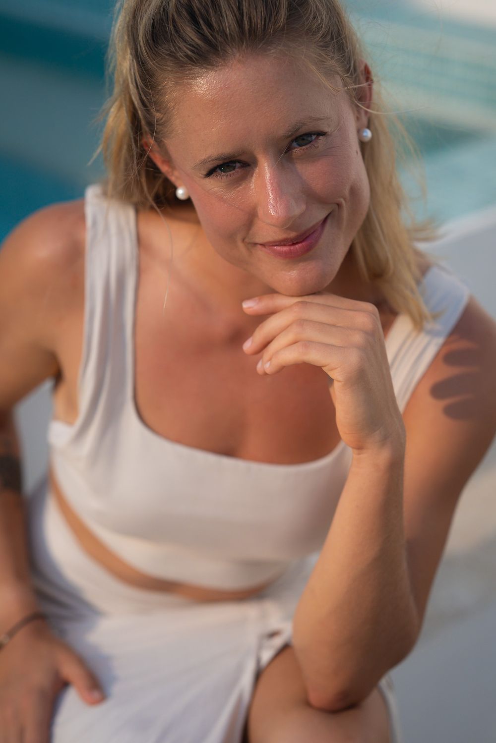 Person wearing white athletic set poses by pool in warm sunlight.