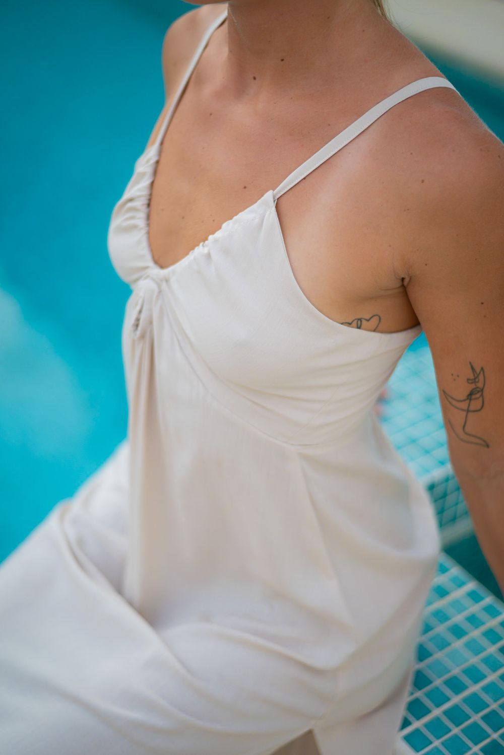 Close-up of white summer dress with thin straps against turquoise pool background.
