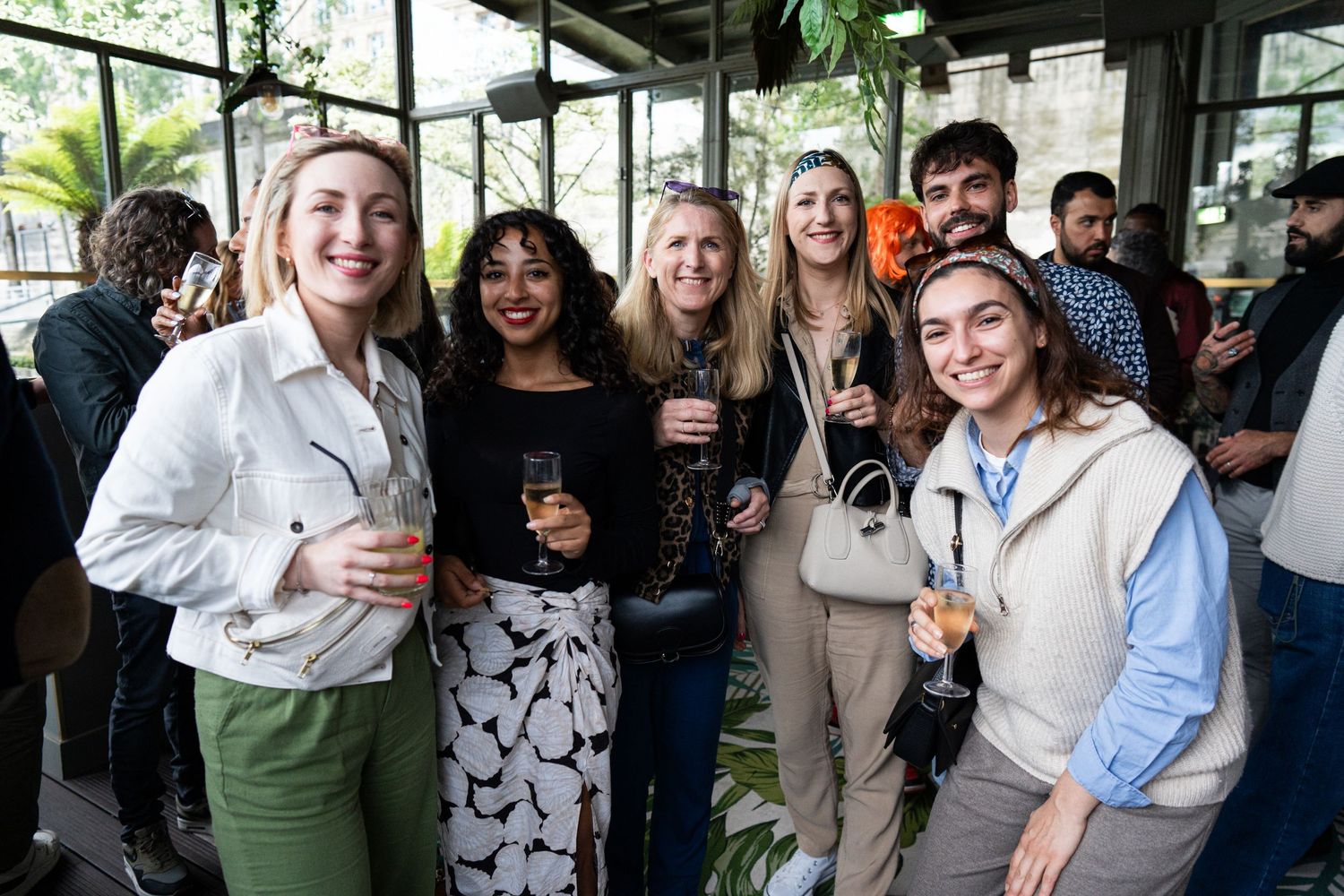 Friends gather together at a social event holding drinks and smiling.