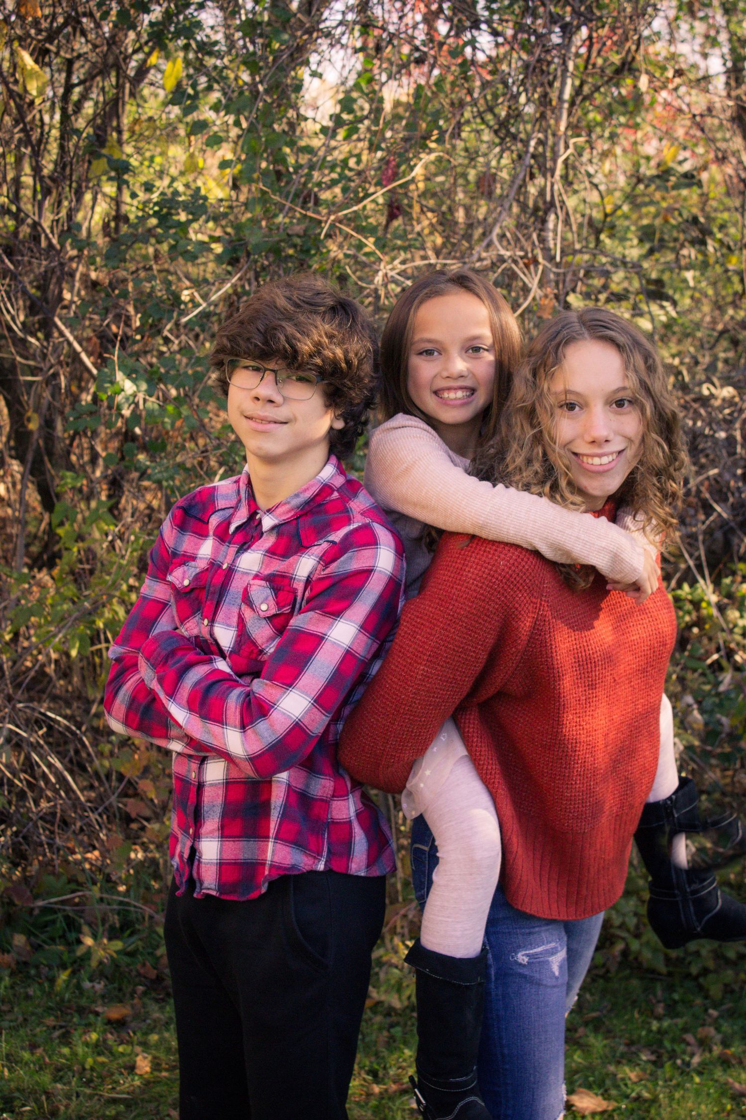A casual outdoor autumn family photo shoot with plaid and knit sweaters against a natural foliage backdrop.
