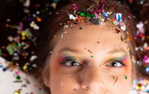 Artistic close-up portrait with shimmering confetti creating ethereal effect against white backdrop.