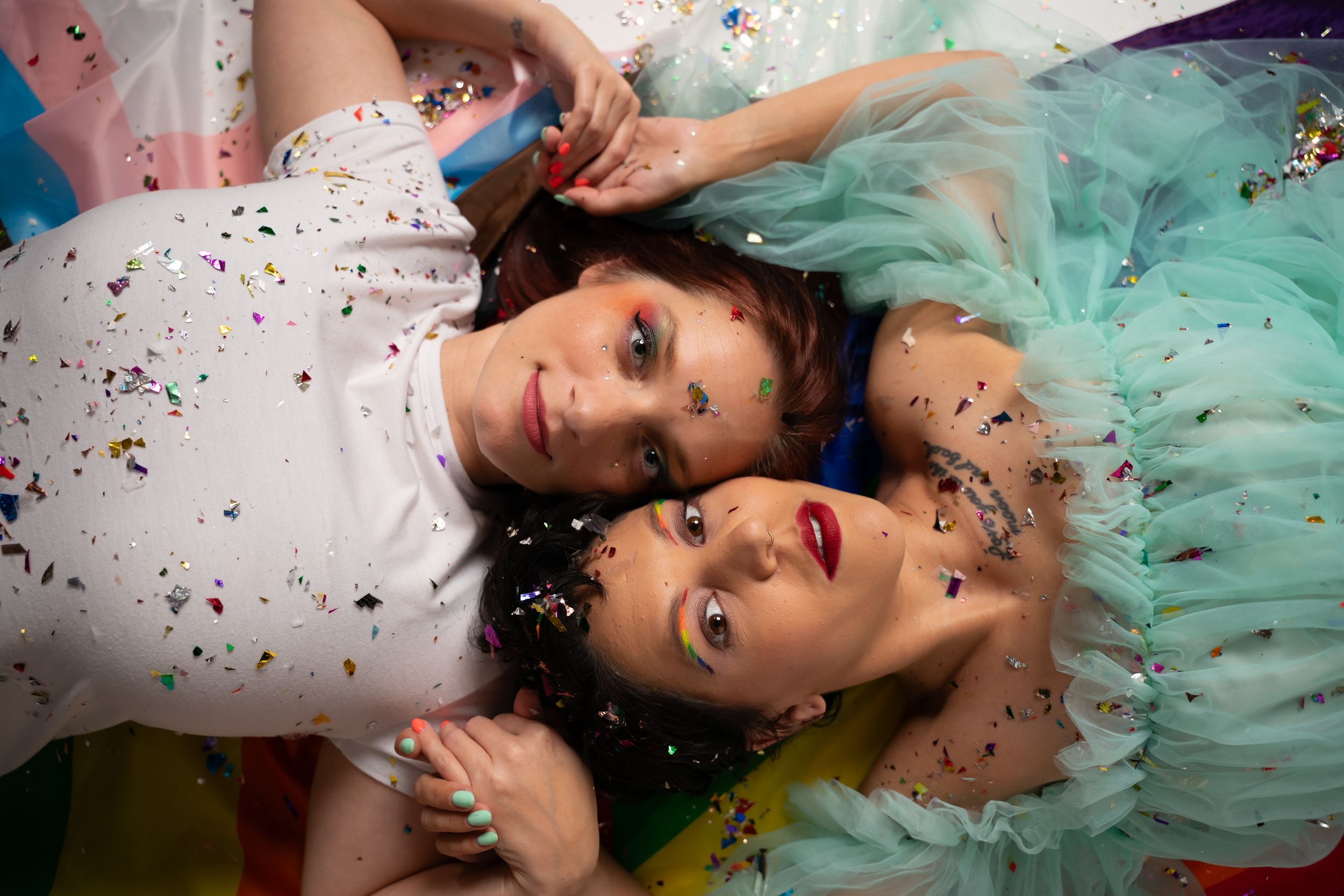Dramatic lying down portrait with scattered confetti and mint tulle dress against white backdrop.