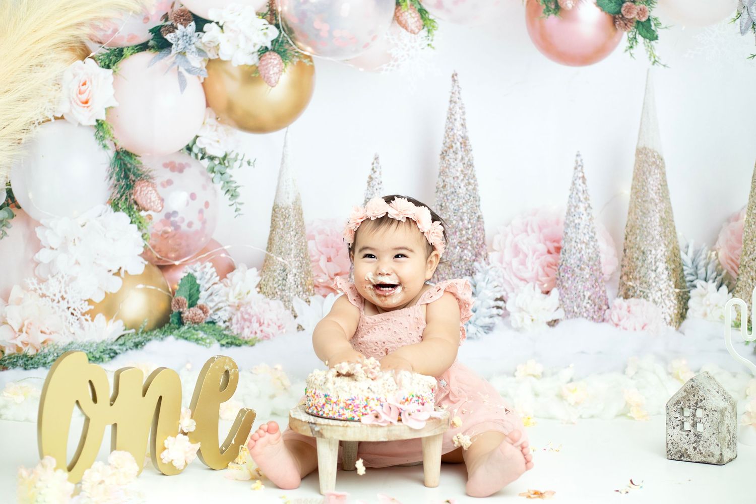 Baby's first birthday cake smash setup with pink and gold winter theme decorations.