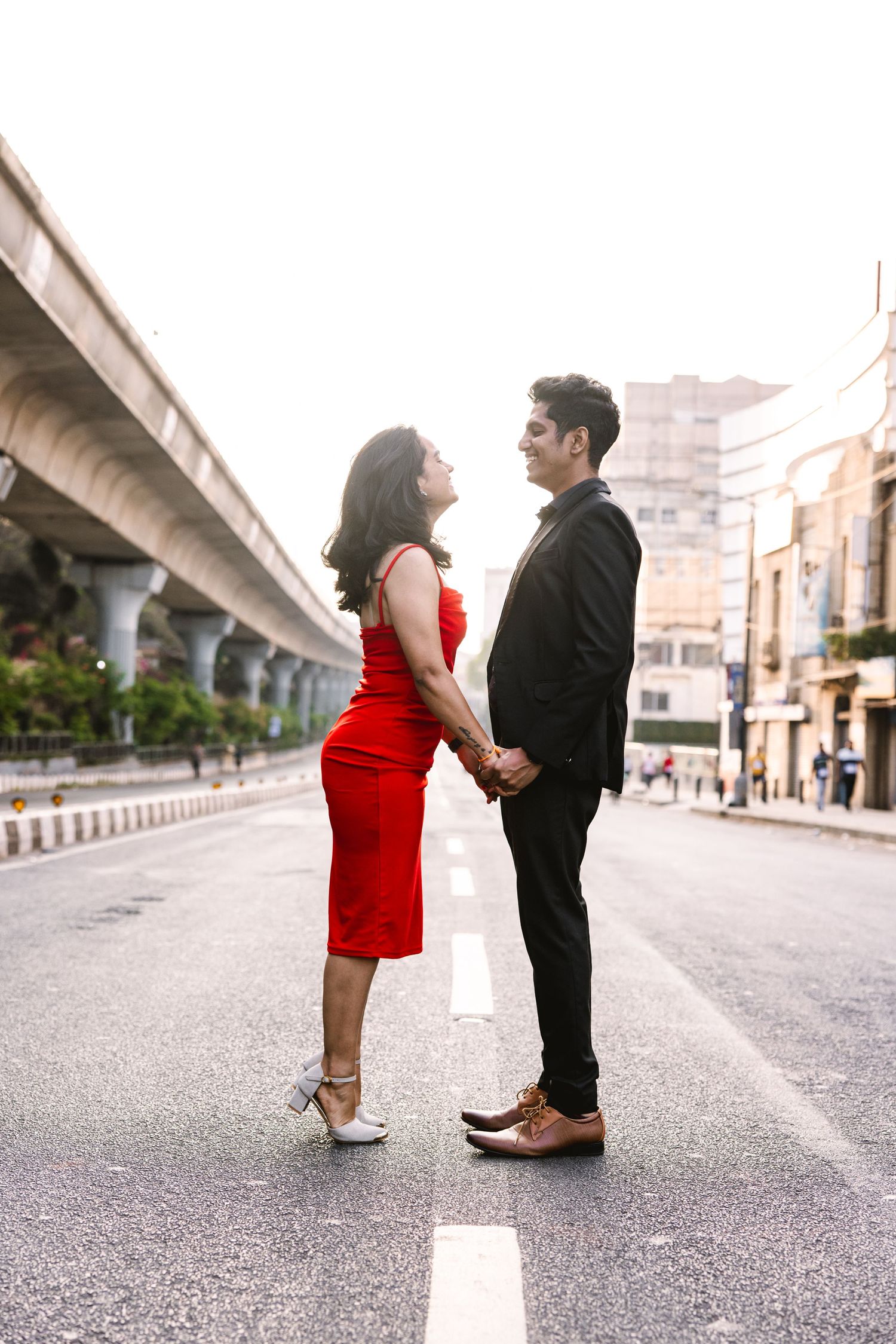 Romantic couple in formal wear standing on city street with overpass in background.