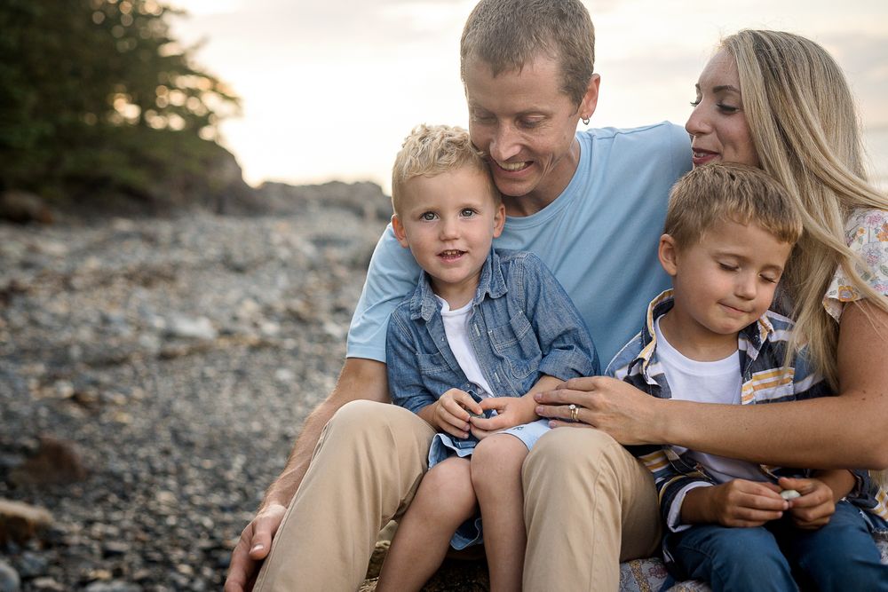 Family relaxing together on rocky beach during golden hour.