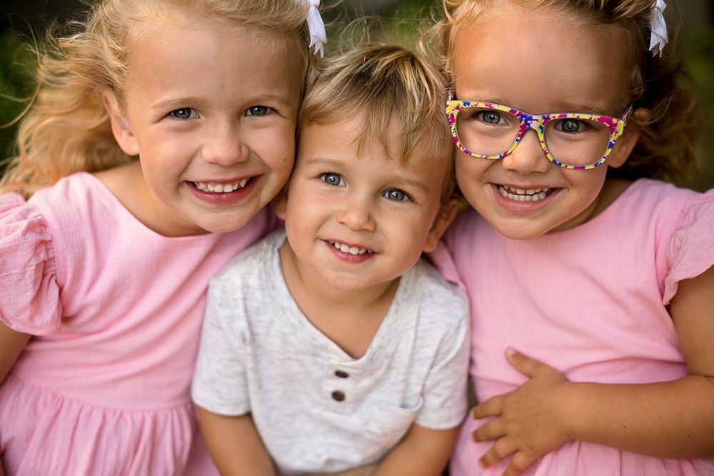 Children wearing pink shirts hugging and smiling together outdoors.