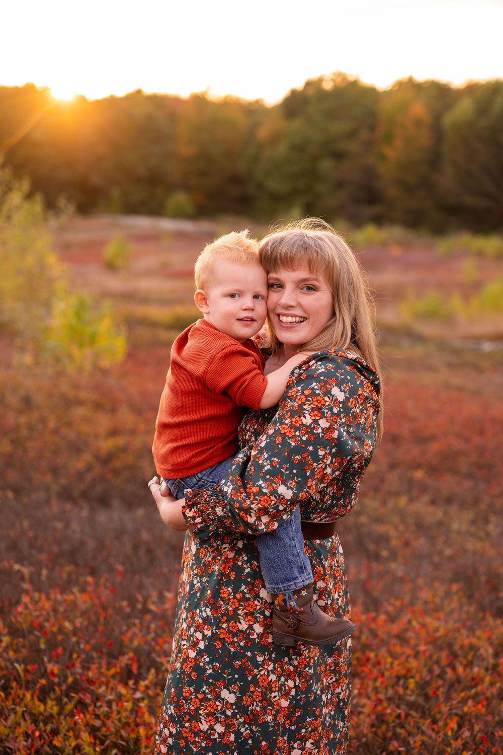 A parent and child share a tender moment at sunset in a field of red autumn foliage.