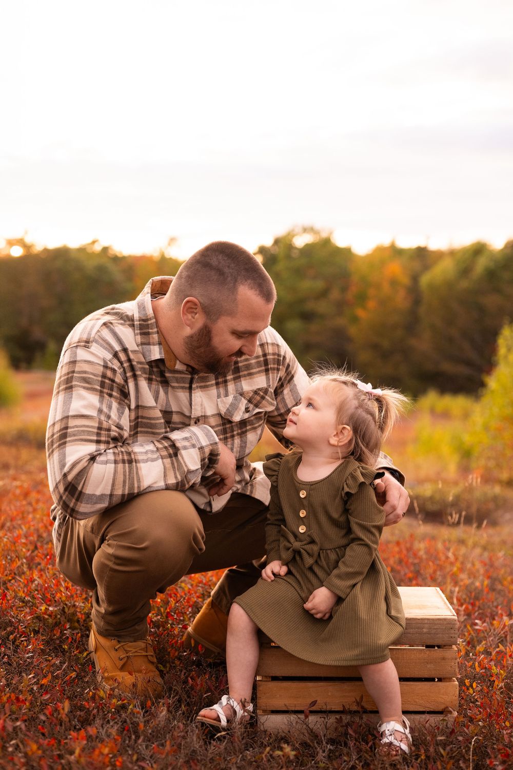 A couple shares a romantic moment on a wooden bench surrounded by autumn foliage at sunset.