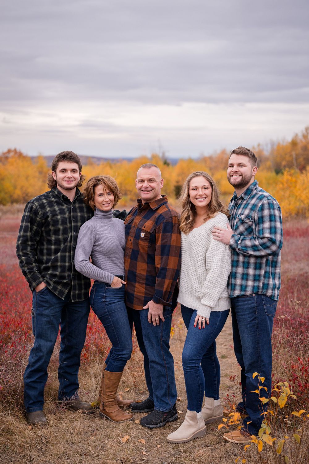 A family group wearing coordinating casual outfits poses together against a backdrop of vibrant autumn foliage.