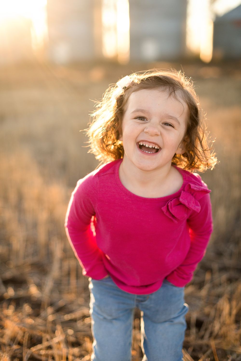 Child in bright pink shirt playing in field during golden hour.
