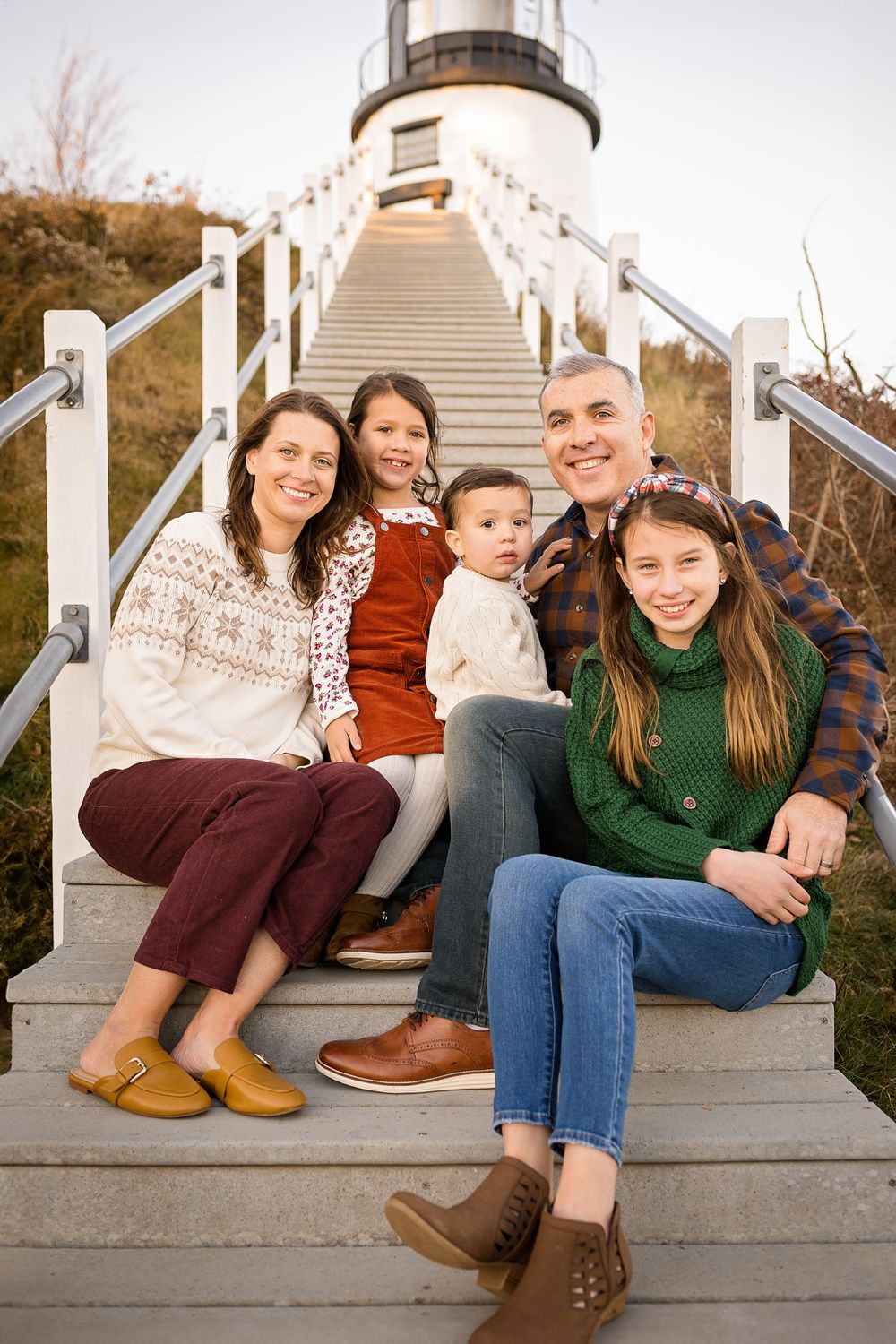 Family sitting together on white wooden steps outdoors in casual fall clothing.