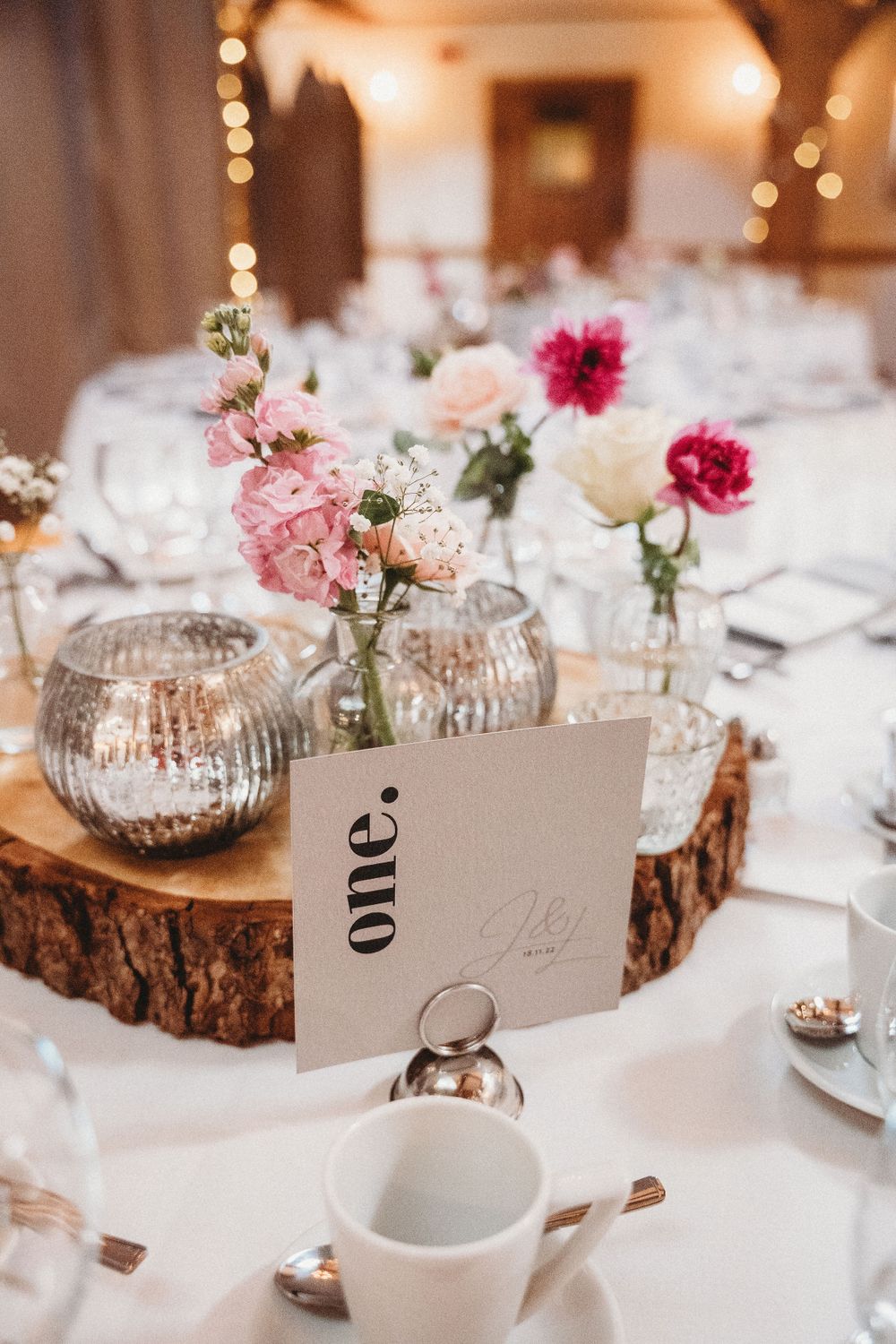 Wedding reception tables decorated with wood slices, flowers and table numbers in elegant setting.