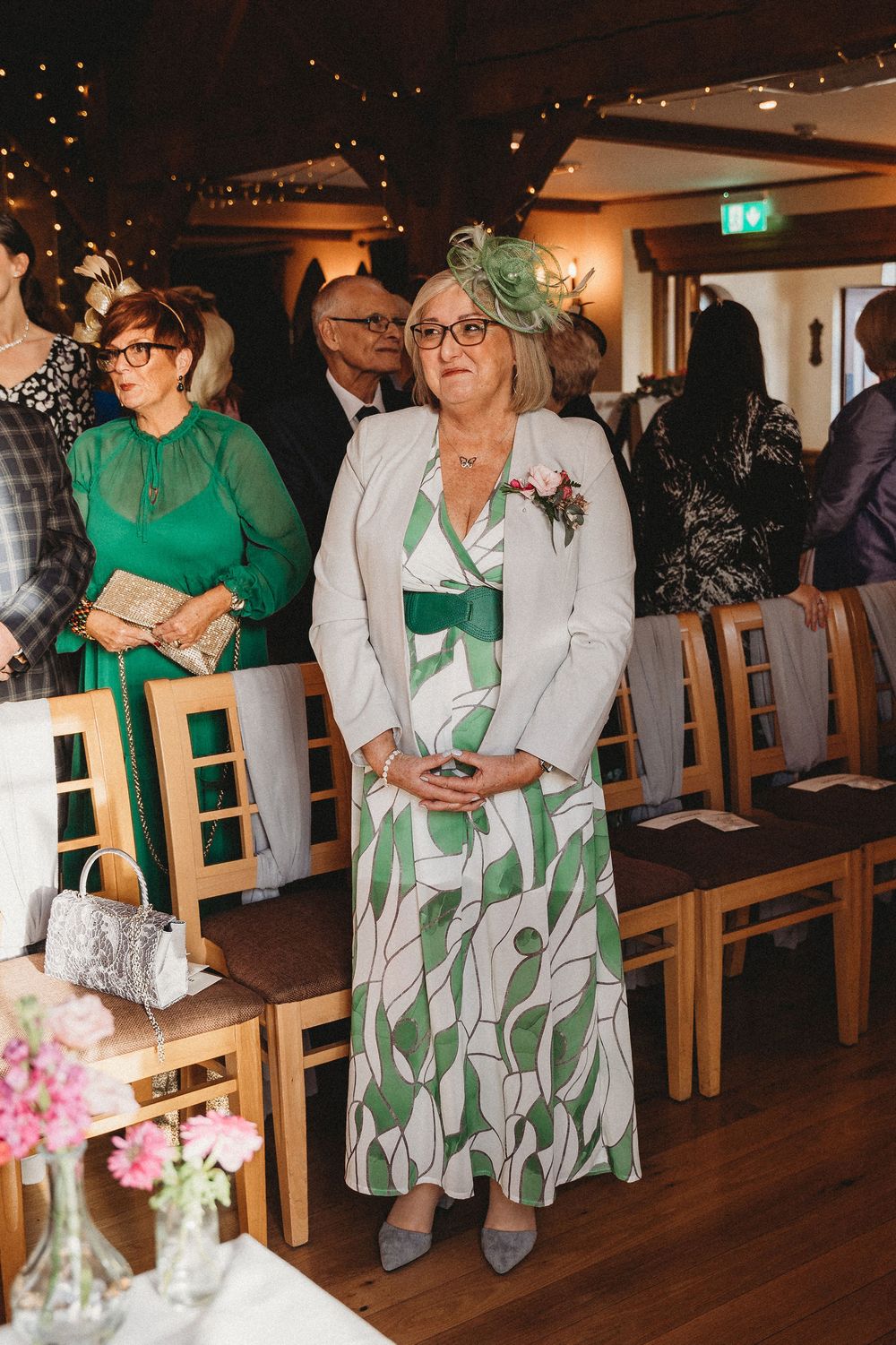 Wedding guests in green dresses seated in wooden chairs during ceremony.