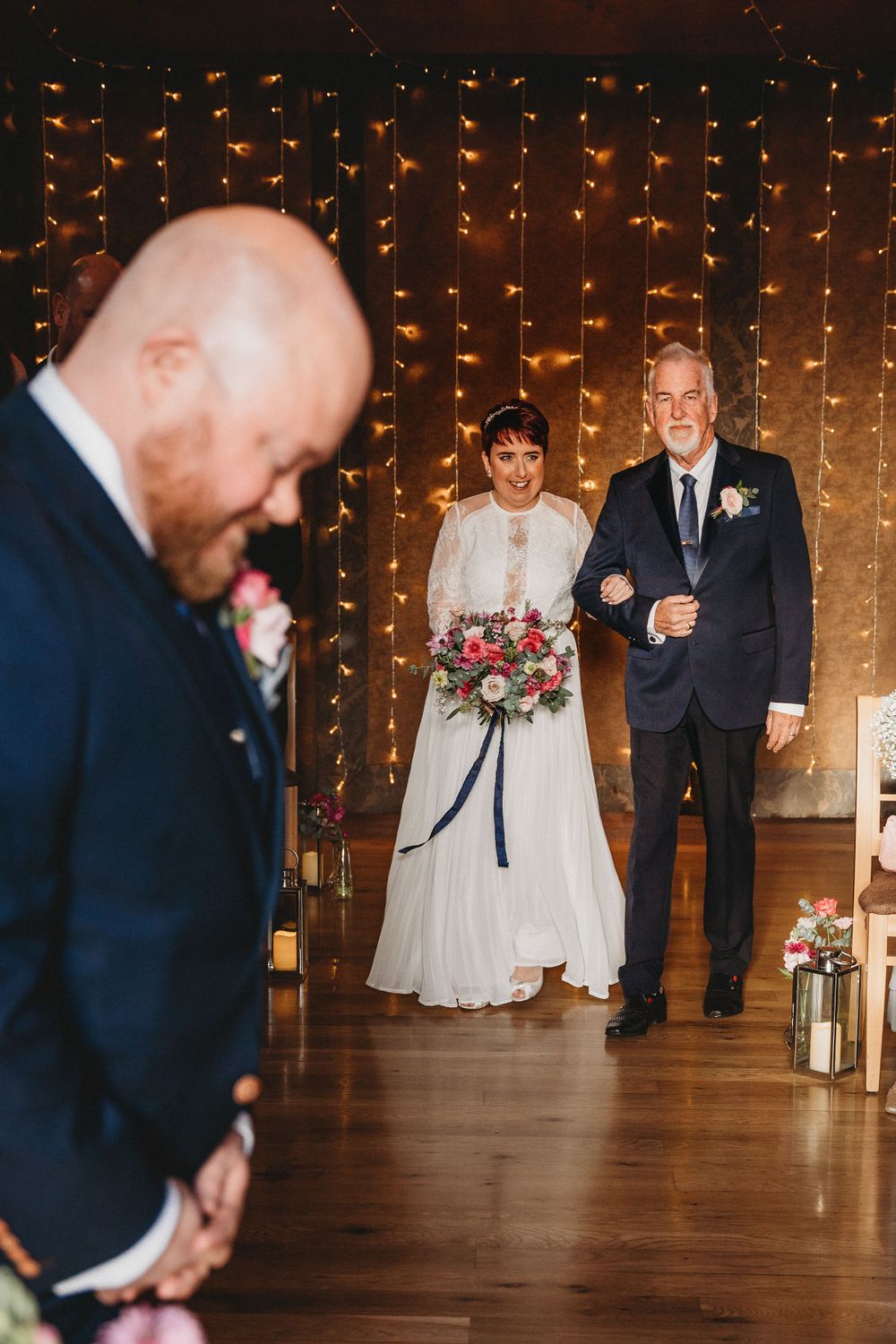 Indoor wedding ceremony with string light backdrop and elegant white dress in focus.