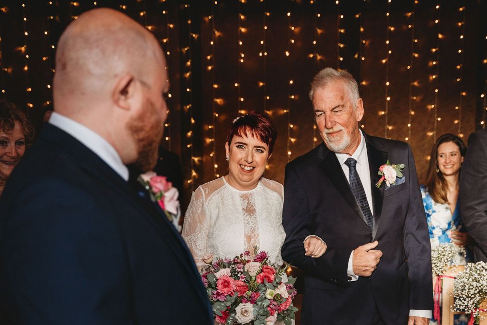 Wedding ceremony space illuminated by string lights with guests seated in rows.