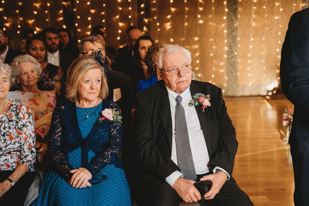 Wedding guests seated at reception tables under warm string lights in rustic barn setting.