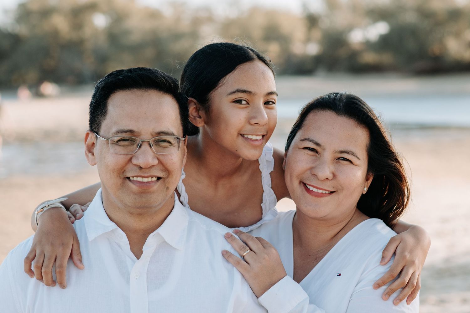 Three people share a warm embrace while posing on a beach at sunset.