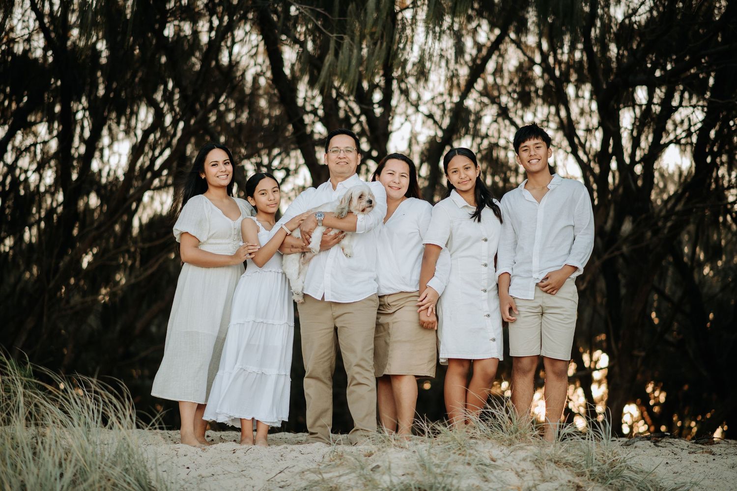 A group wearing coordinated white outfits poses outdoors among trees and natural scenery.
