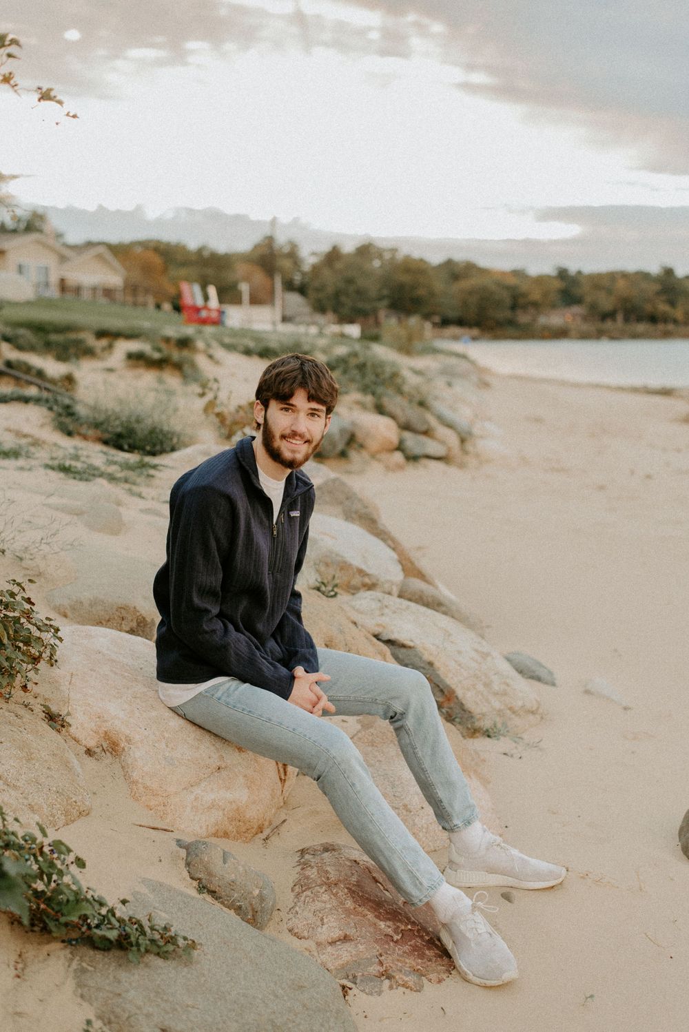 A person in casual wear sits on coastal rocks during sunset.
