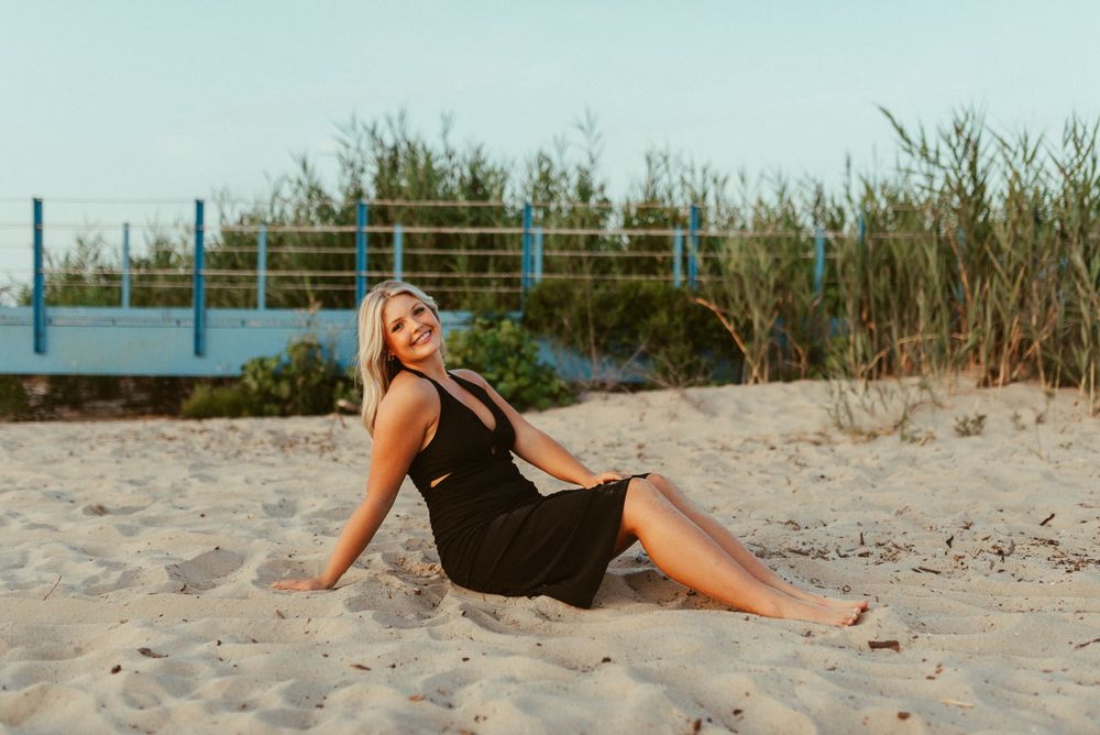 A person in black reclines on beach sand during a coastal photoshoot.