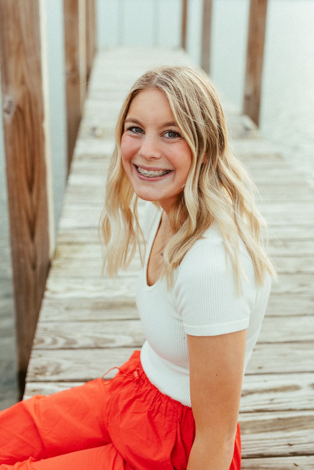 Portrait of young woman in white top and orange skirt smiling on wooden boardwalk.