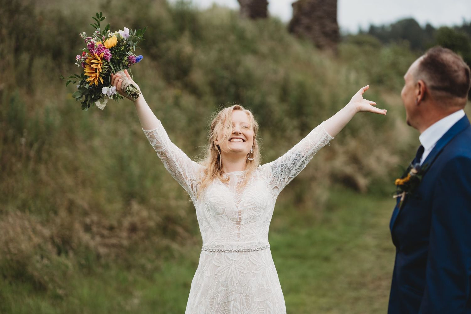 Bride embracing the rainy weather with arms outreached and bouquet in one hand and eyes closed.