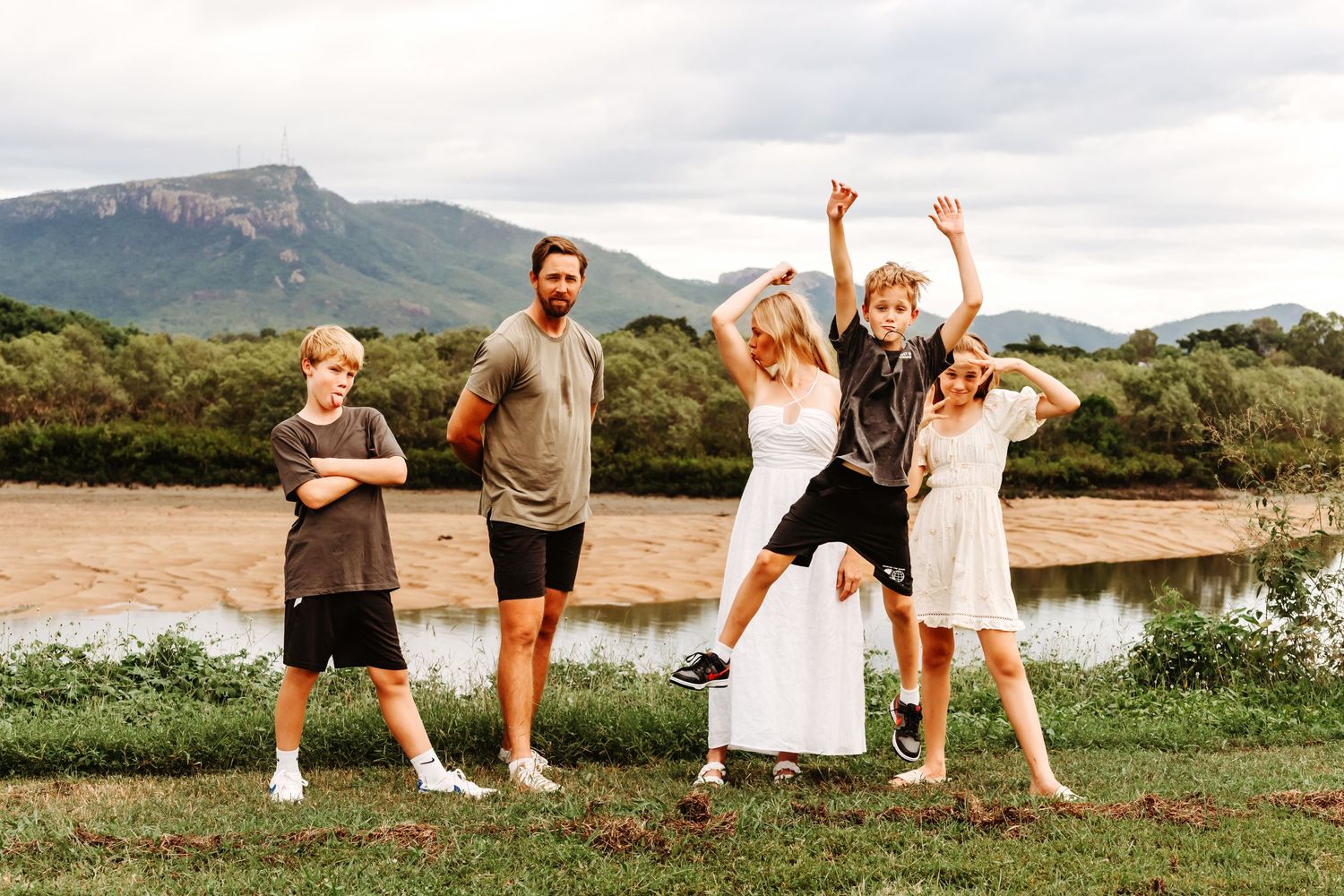 A group celebrates joyfully in an outdoor setting with mountains and a river in the background.