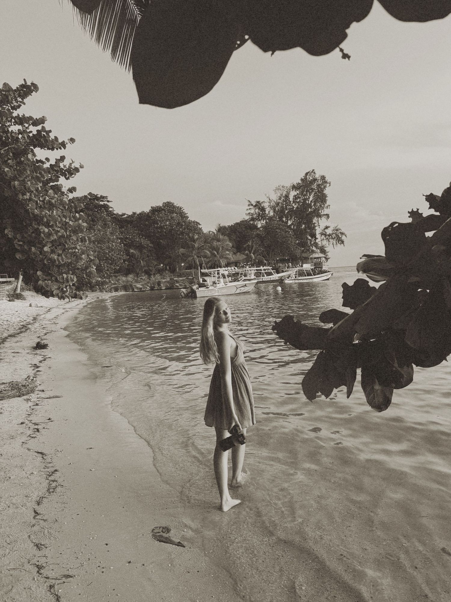 A black and white photograph of someone walking along a serene beach shoreline.