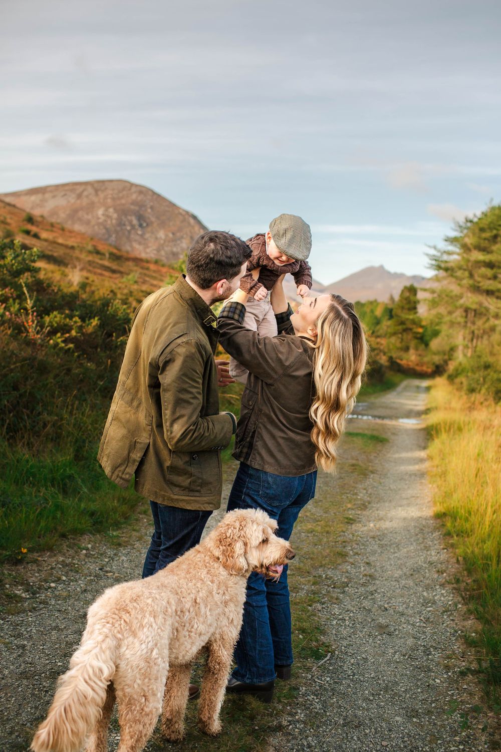 Family and their goldendoodle dog sharing a tender moment on a mountain path at sunset.