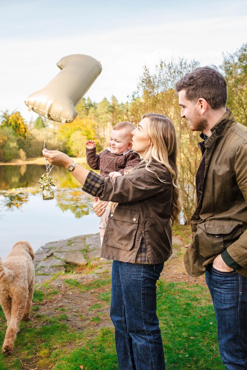 A family and their fluffy dog play together by a lake on an autumn day.