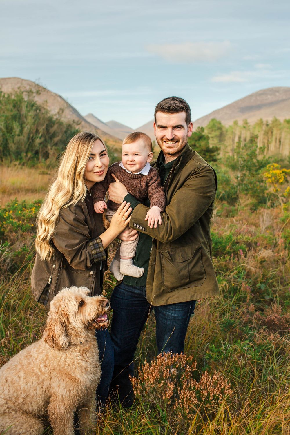 A happy family poses with their fluffy dog against a mountainous landscape.