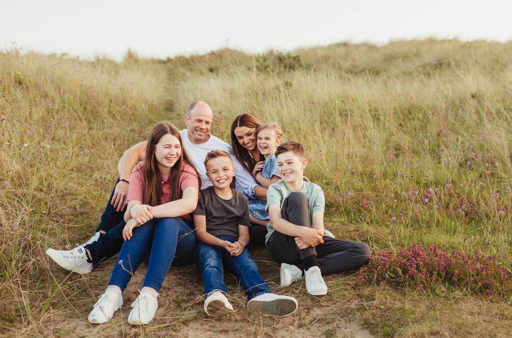 Family relaxing together on grassy hillside during outdoor photo session.