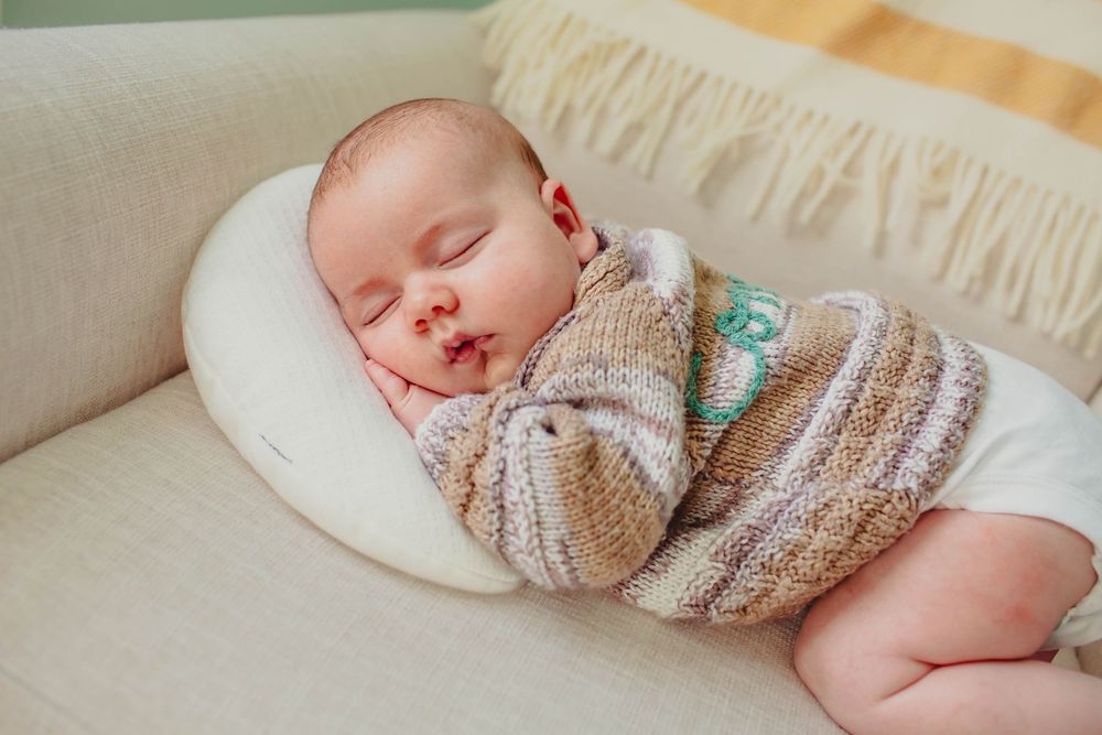 A sleeping newborn baby wrapped in a knitted blanket on white bedding.