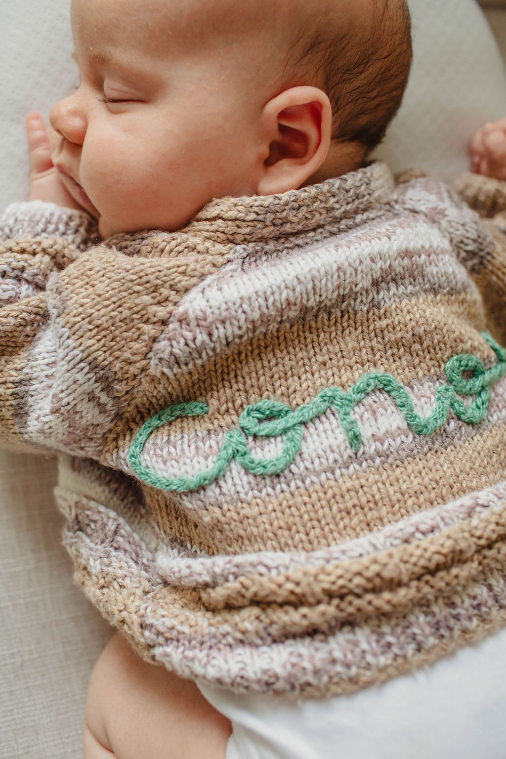 A peaceful newborn sleeps wearing a handknit sweater with mint green accents.
