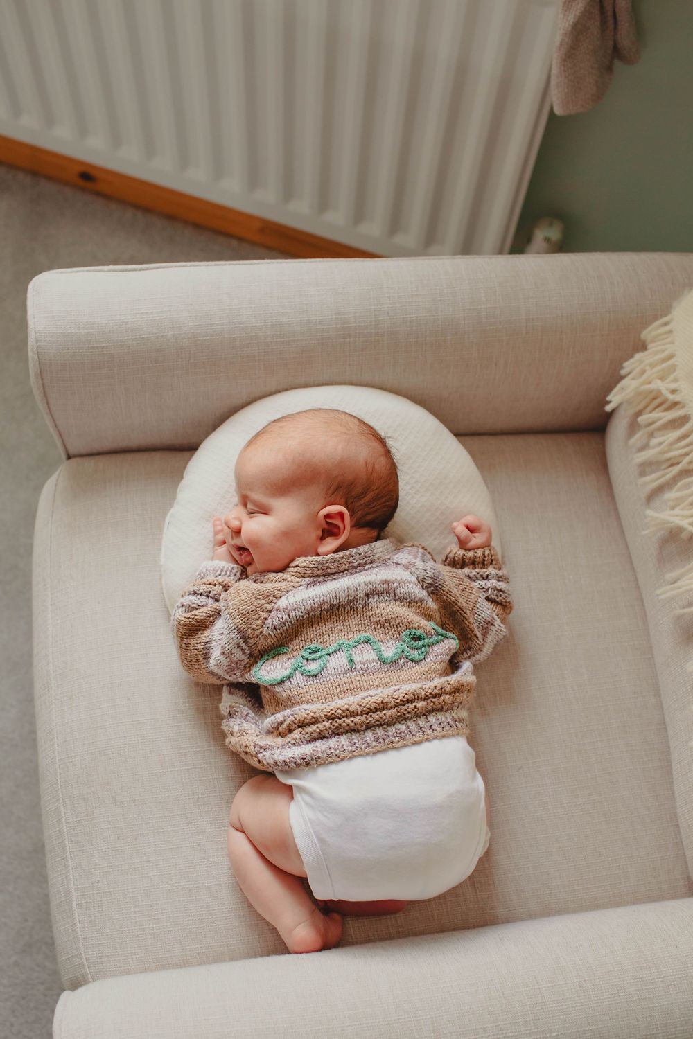 Sleeping baby wearing cozy sweater rests peacefully on beige armchair.