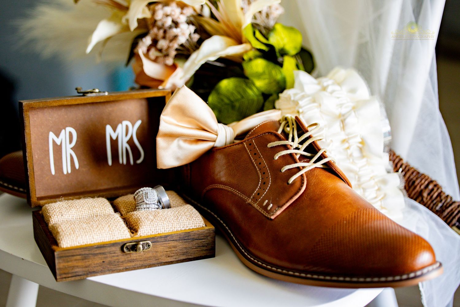 Wedding details including brown leather shoes and wooden Mr & Mrs sign arranged with floral accents.