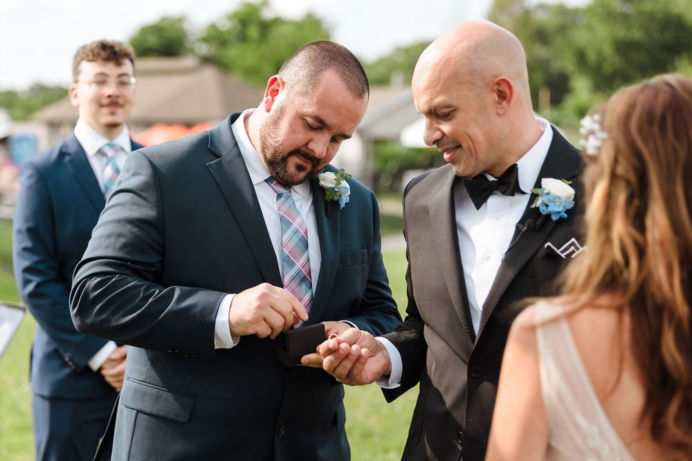 The best man hand's the groom the wedding band for the exchanging of rings during an outdoor ceremony