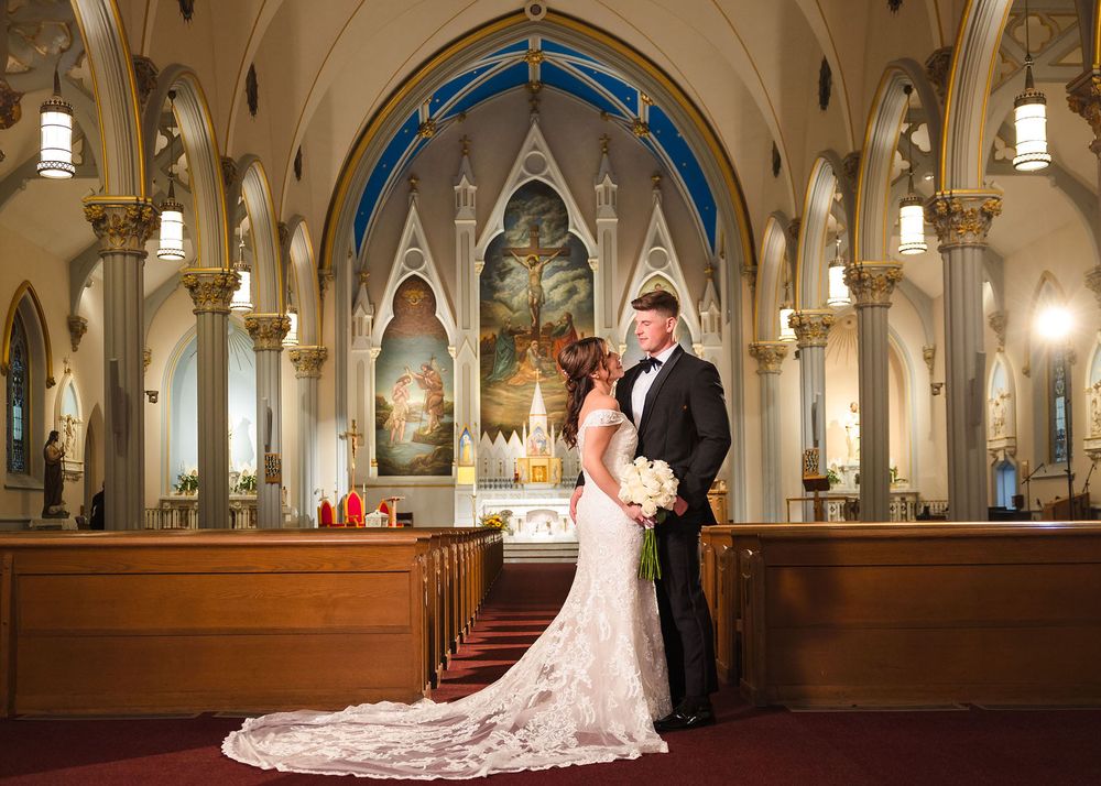 The bride and groom pose for a formal portrait inside a beautiful catholic church in Boston's North End