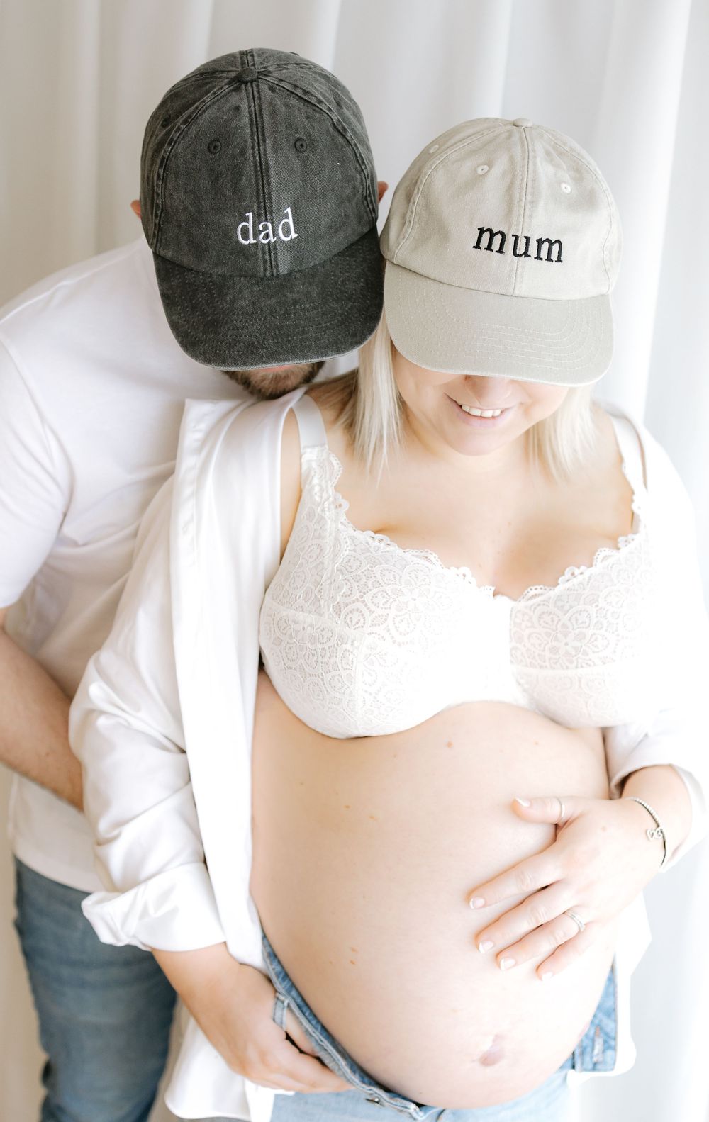 Expecting couple wearing dad and mum baseball caps during a maternity photoshoot, showing baby bump.