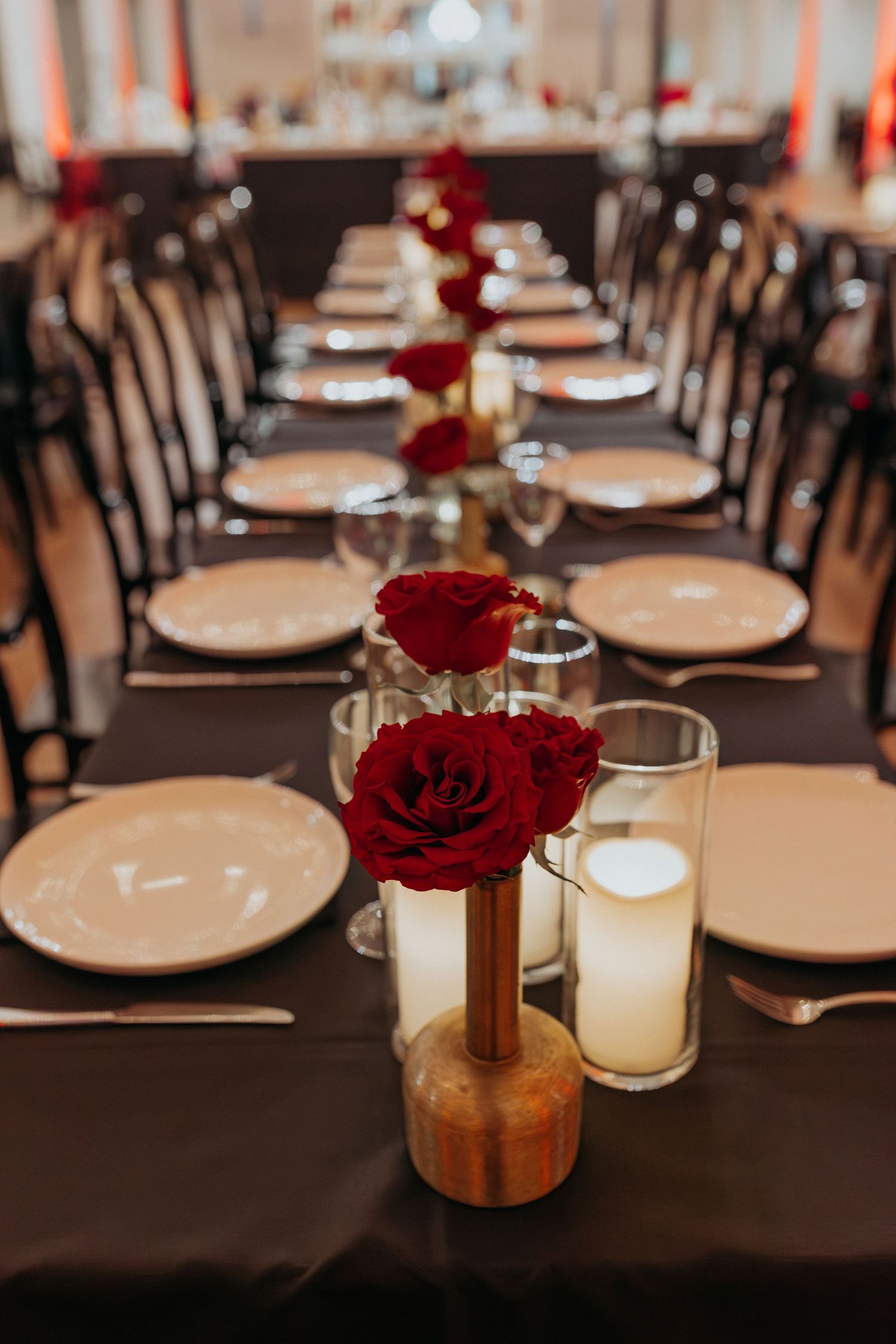 A long table set with plates, candles, forks, knives, and roses.