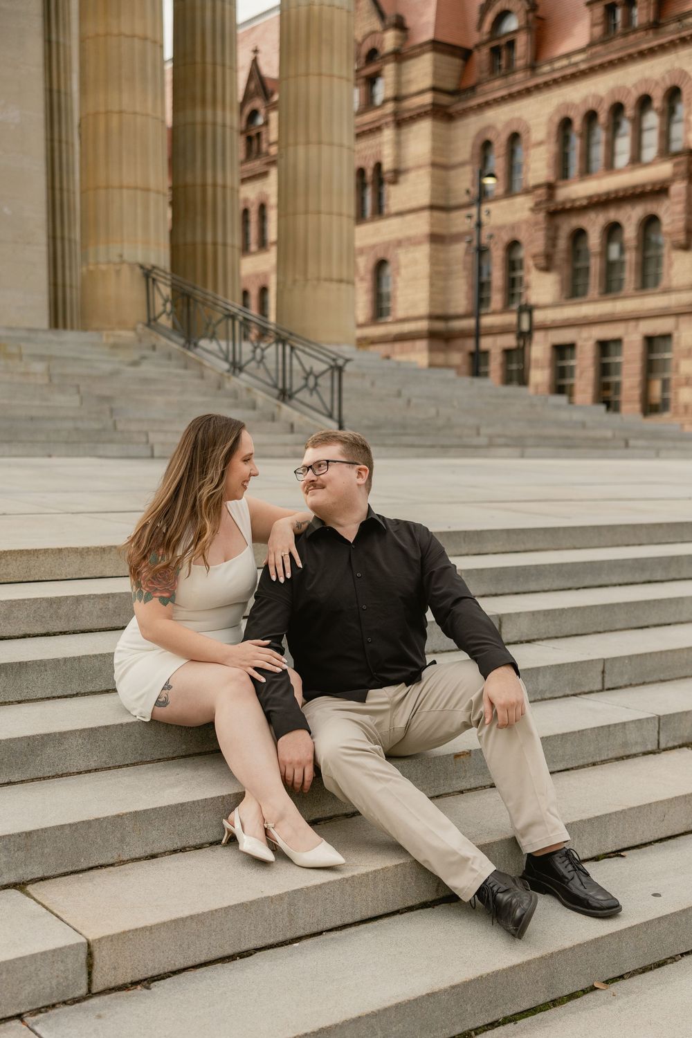 A couple sits intimately on stone steps of a historic building with columns in warm afternoon light.