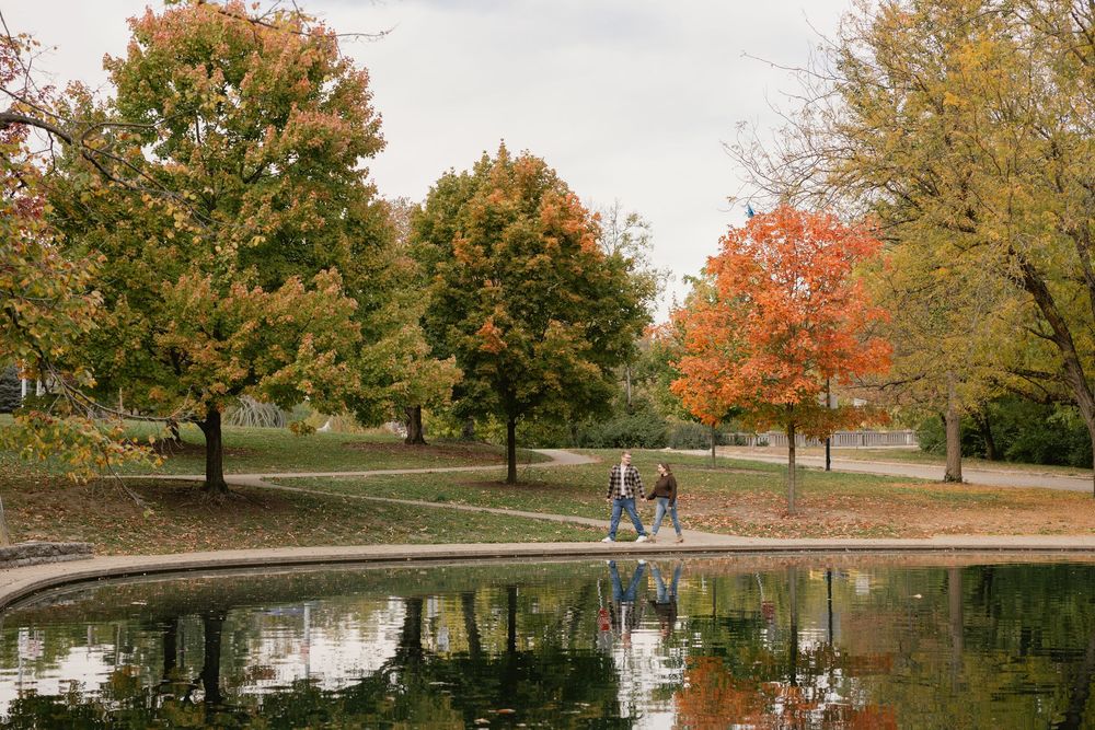 Scenic autumn park path along a tranquil pond with colorful fall foliage reflecting in the calm water.