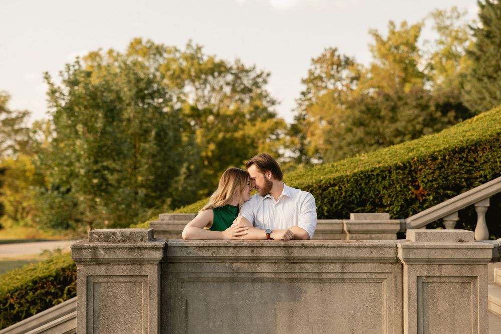 A couple shares a romantic moment on a stone wall during an outdoor engagement photo session at sunset.