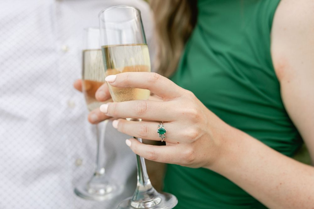 A hand wearing an emerald ring holds a champagne glass during a celebration.