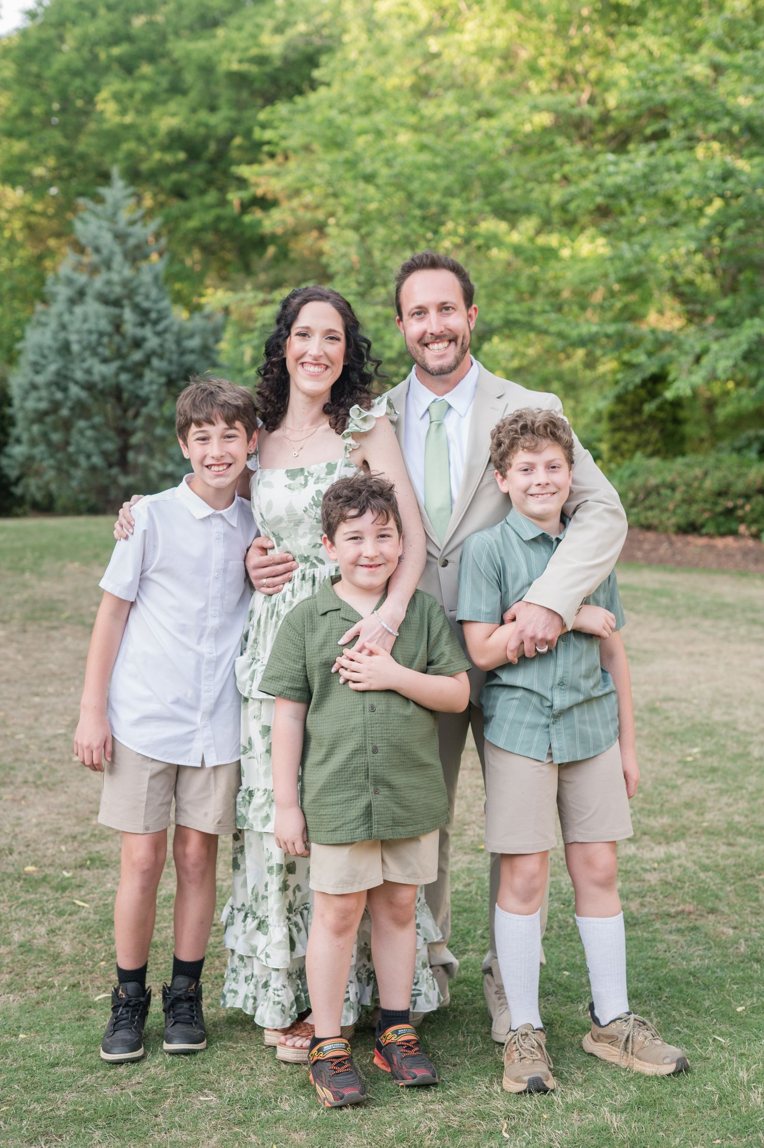 A family plays and laughs together on a grassy hill near a serene lake on a sunny summer afternoon.